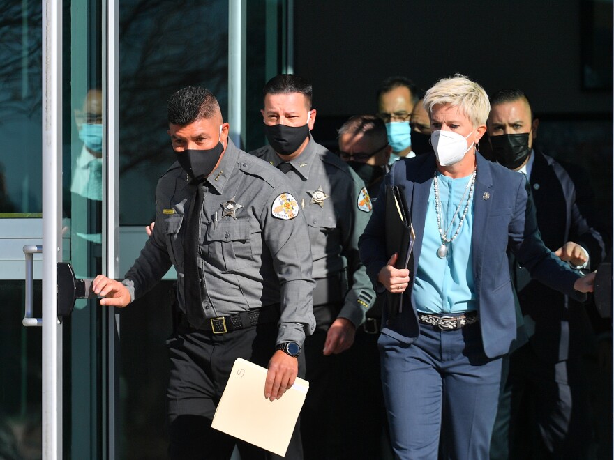 People in law enforcement uniforms and civilian clothes exit a building with masks on.