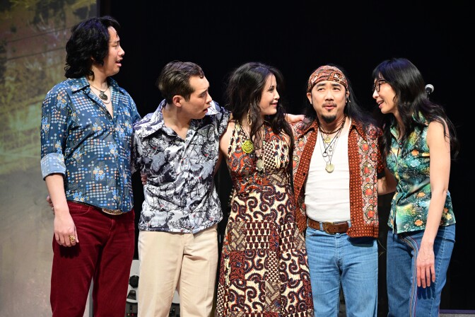 A group of three men and two women dressed in a colorful, busily-patterned shirts and jeans. 