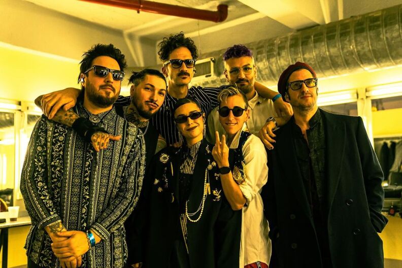 The seven members of the band Siamés pose for.a photo backstage at one of their shows. There's a yellow hue to the image.