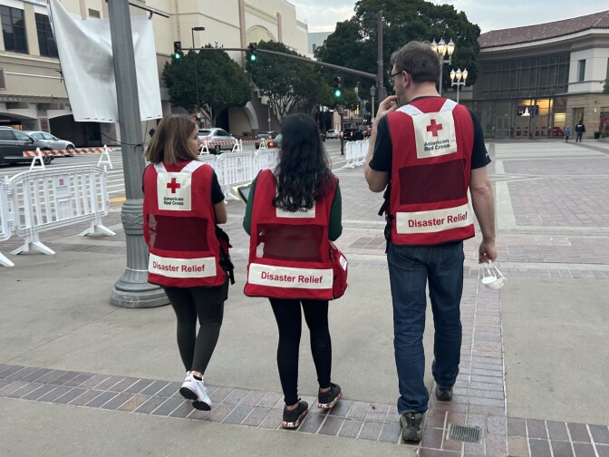 Three people wearing Red Cross disaster relief vets walk together away from the camera.
