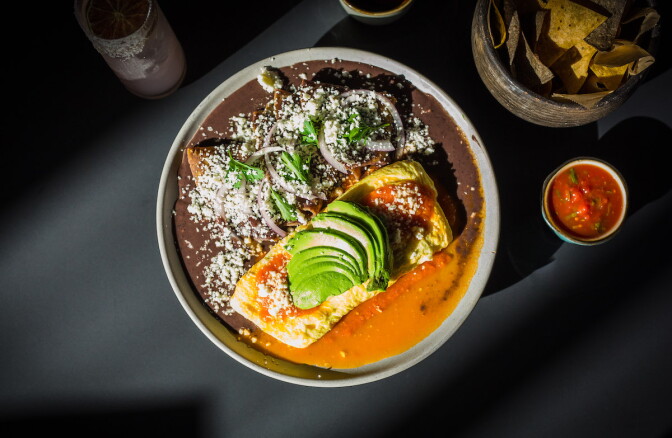 An omelette topped with avocado with black beans and salsa on the side.