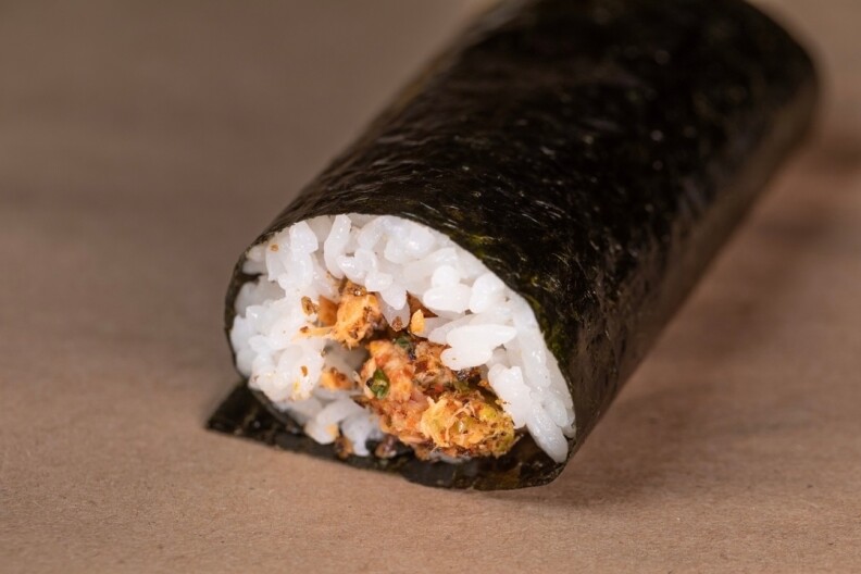 A well-prepared handroll is displayed on a light brown surface.
