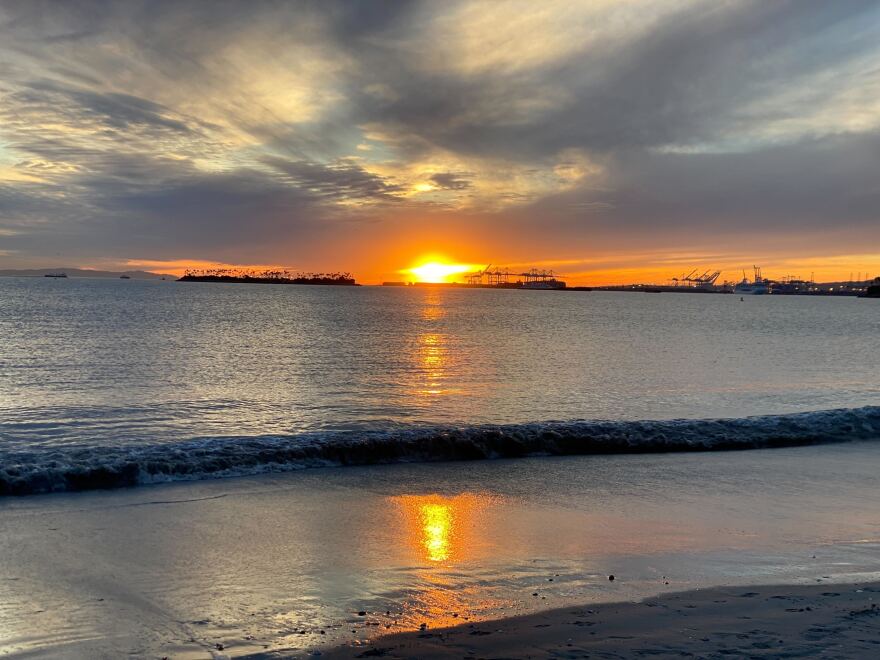 A setting sun melts into the sea beyond the ports.