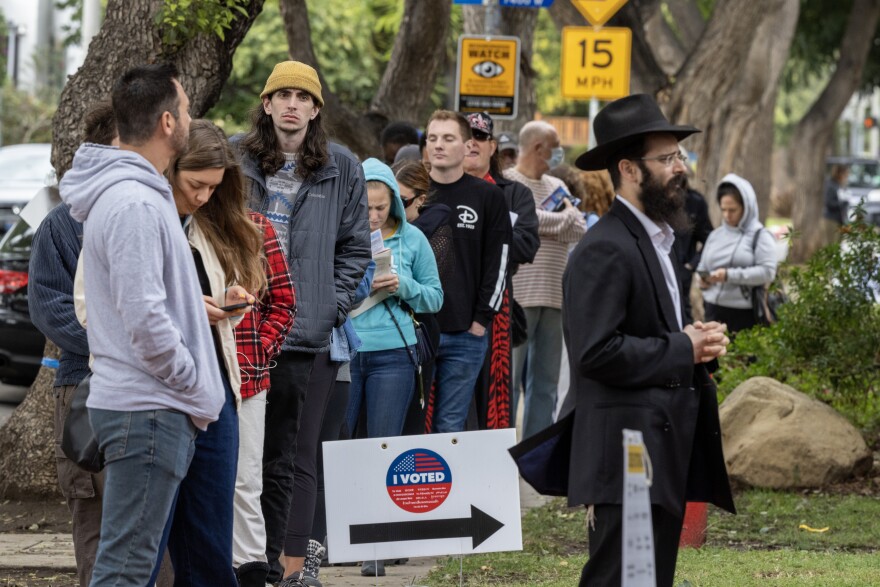 A line of people wait to vote by a sign with "I voted" and an arrow.
