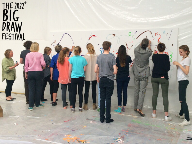 A small crowd of people drawing on a poster hung up on a white background.