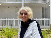 Sumaiyya Evans is photographed in the courtyard of her apartment building. She's wearing sunglasses and a black shirt with a white shawl.