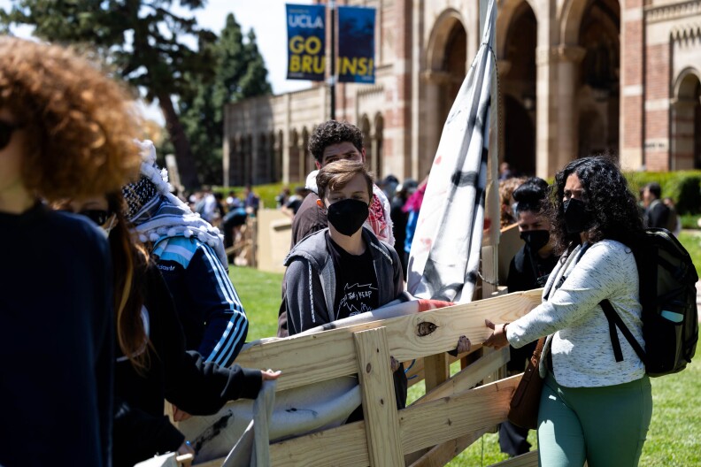 A group of people carry wooden beams on a lawn.