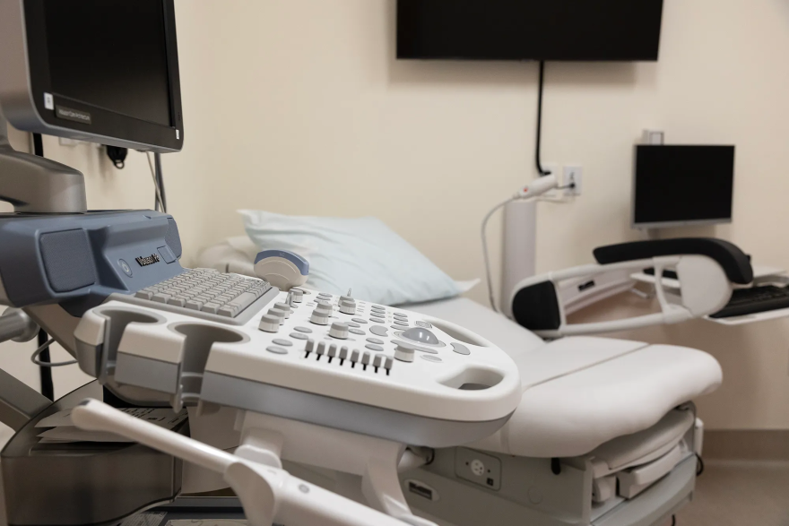 A medical examination room with a bed, video screens and monitoring devices
