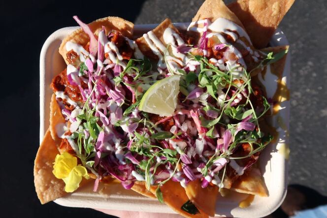 A light skin hand holding a plate of nachos with slaw and lime.