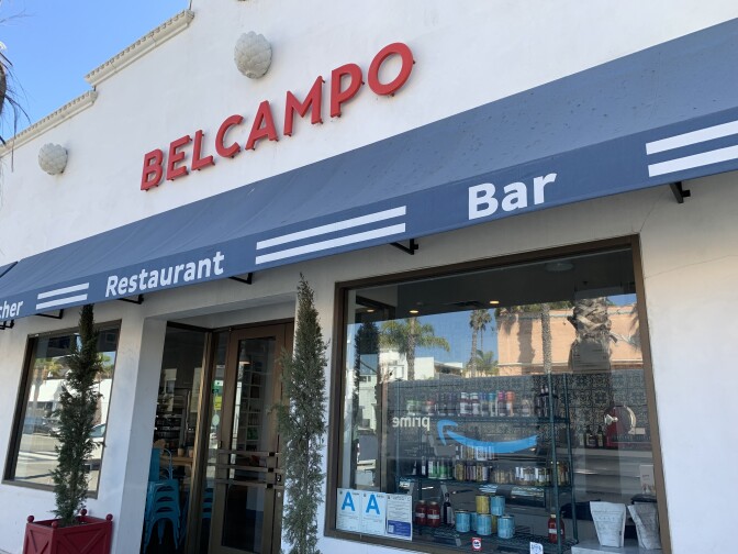 letters on a building read "BELCAMPO" above a blue awning overlooking store windows