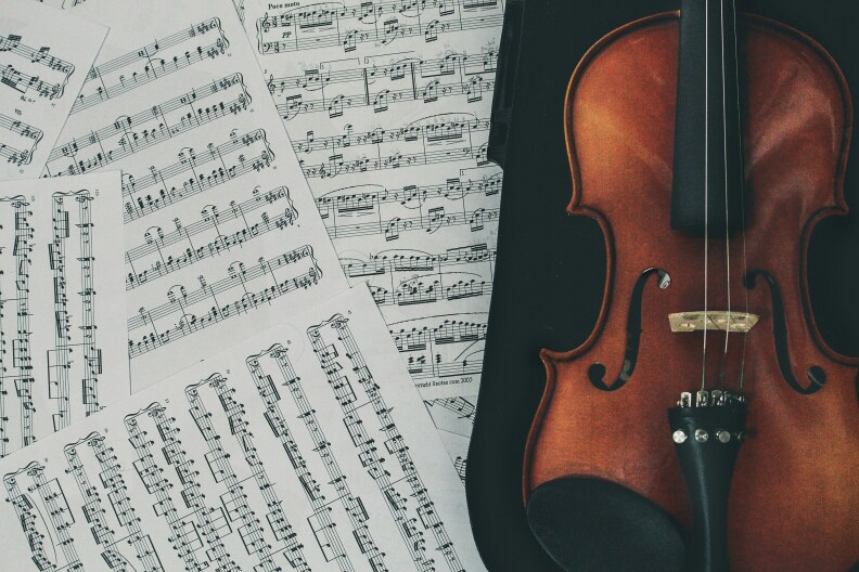 Pages of sheet music are strewn on the left side of the frame while a violin rests on the right side.