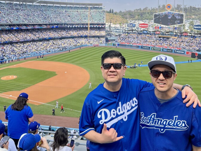 Two Asian American men in Dodgers jersey pose at the stadium. 