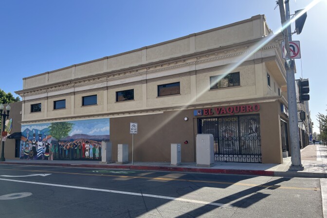 A street corner with a shop closed up for the day with metal fencing protecting its windows. There are no people in sight.