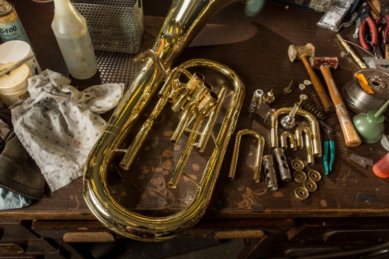 A baritone rests on the table of a technician in the early stages of the repair process.