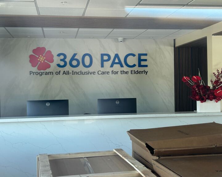 The interior of a business in transition — packing boxes are lined up, but there are welcoming flowers in the reception areas and computer monitors. Signage reads: "360 PACE Program of All-Inclusive Care for the Elderly"