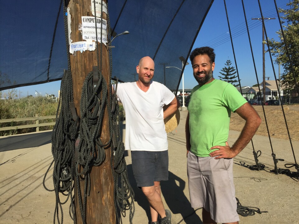 Joshua Callaghan, left, and Daveed Kapoor, right, with their sculpture, Mast, which is part of LA's public art biennial, CURRENT:LA. The sculpture is made of an actual telephone pole, complete with neighborhood flyers.