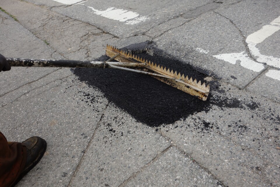 Loose asphalt is raked across a pothole