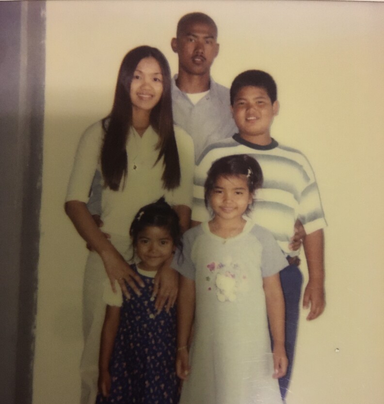An old photo shows a young Asian man in a blue shirt standing behind three younger girls and a boy.