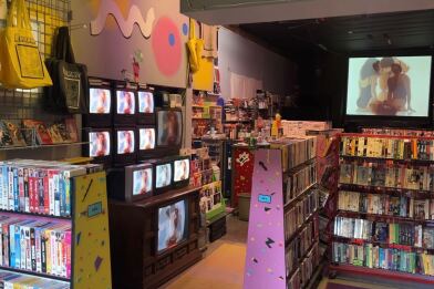 A view inside Whammy Analog Video. Countless VHS tapes can be seen lining the walls. A large projected screen is in the background. A row of old CRT Televisions sit on the left side of the picture.