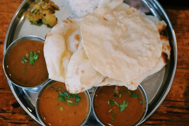 A plate of naan and papadum with small metals carafes of curries and dips.