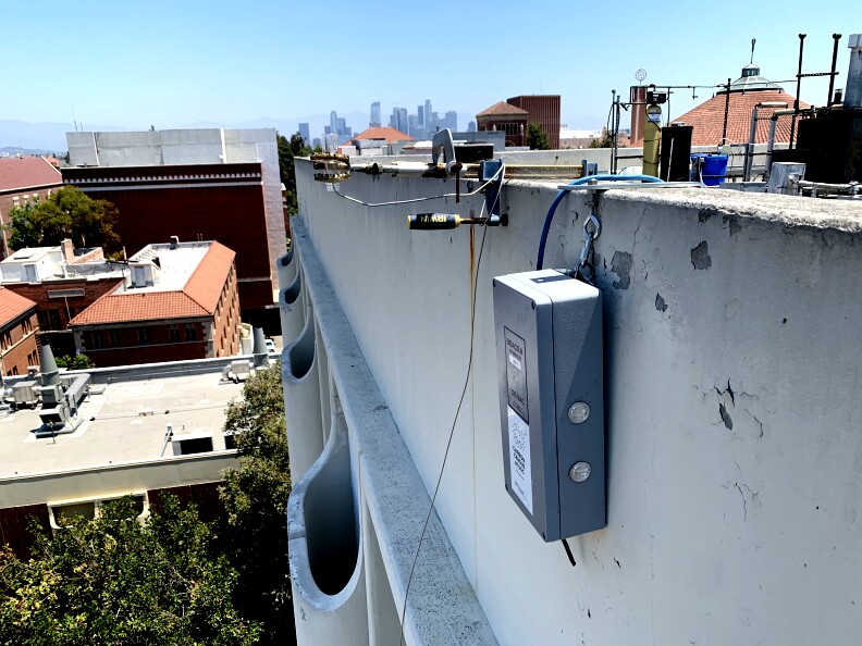 The grey shoebox sized sensor hangs on the side of the building, ready to collect pollution data.