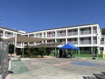 A three story white motel building with green accents and pink doors that's been converted to a family shelter. 