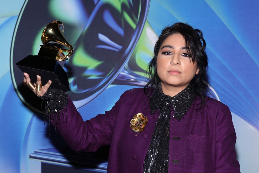 Arooj Aftab in a deep purple kacket hold up the Grammy with her right hand.