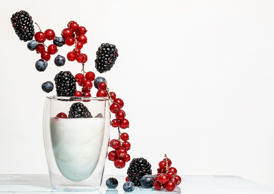 Blackberries, blueberries and red currants fall into a glass cup of yogurt