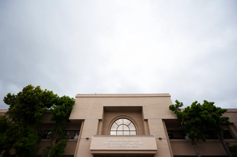 A low angle view of a building with trees in front of it and signage in the center above an entrance that reads "Hollywood courthouse. Superior court of California. County of Los Angeles."