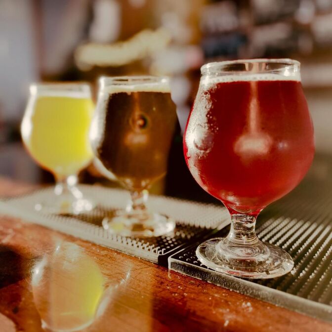 Three bulbous glasses of beer lined up on a bar, one light, one amber and one dark. 