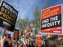Picketers hold high red, yellow and black strike signs. They read: "Stand with Kaiser therapists" and "Patients before profits" 