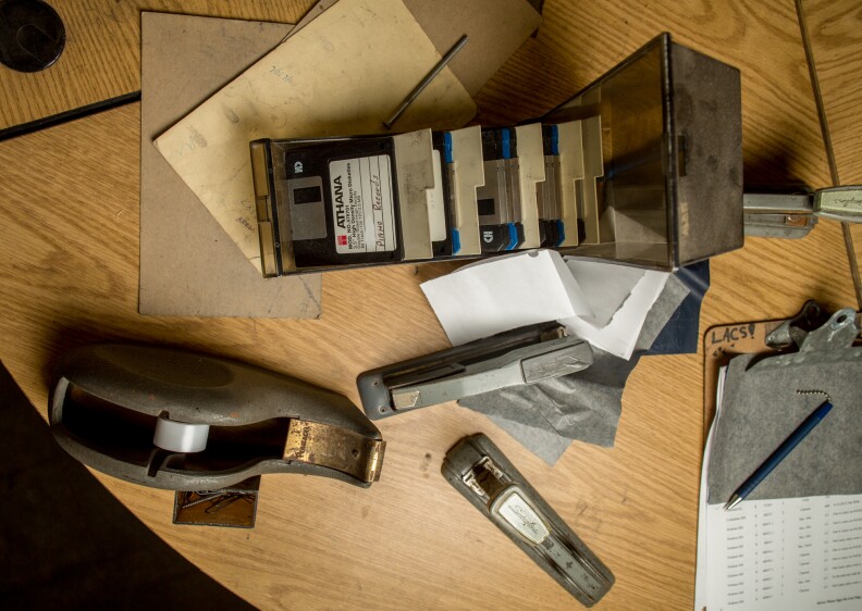 A tray of floppy disks, one reading "PIANO RECORDS" on the label, sits next to a computer in the main hall of the LAUSD Music Repair Shop.