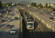 A huge multi-lane freeway full of cars is split down the middle by a Metro train and its tracks.