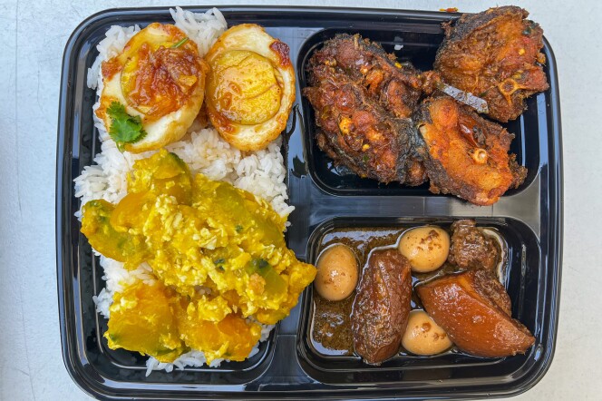 A black plastic to-go tray with three different compartments, each filled with varying types of food. On the left is a bed of cooked white rice containing chunks of an orange squash-like vegetable in a yellow sauce towards the bottom of the tray. On top of the rice are two hard-boiled eggs with a light reddish-brown sauce. The right side has two smaller sections. The top section is filled with large chunks of sliced fish in a dark red sauce, while the bottom section contains large chunks of brown cooked meat and small quail eggs in a light brown liquid sauce.