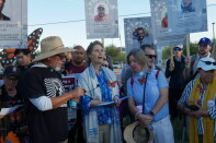 About a dozen people—including interfaith leaders in vestments—stand together along street. They carry signs with faces of different people under the label "died in detention." Some of them have faux monarch butterflies pinned to their clothes. 