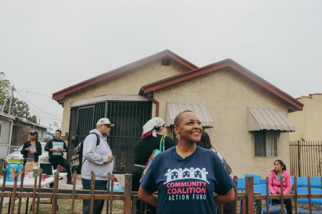 A smiling woman wearing a blue shirt that says "Community Coalition Action Fund" stands in front of a beige house. 