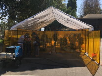 A white tent in a parking lot provides shade to students who are practicing their welding. 
