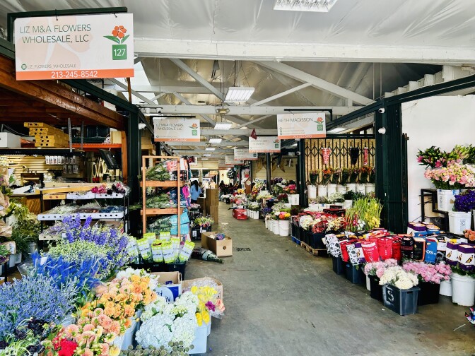 The interior of a warehouse like building which houses multiple stalls. Each stall has buckets of multi colored flowers, stretching as far as the eye can see.