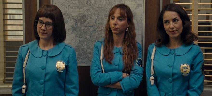 Three women stand in light blue uniforms and police badges.