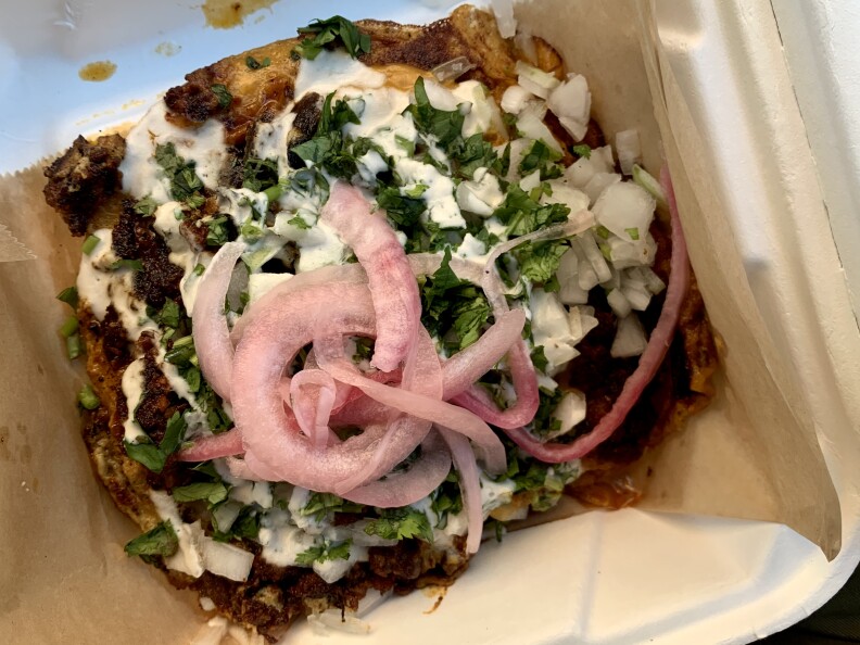 a pile of vegan protein drizzled with white sauce and topped with cilantro, chopped raw onions and pickled onions.