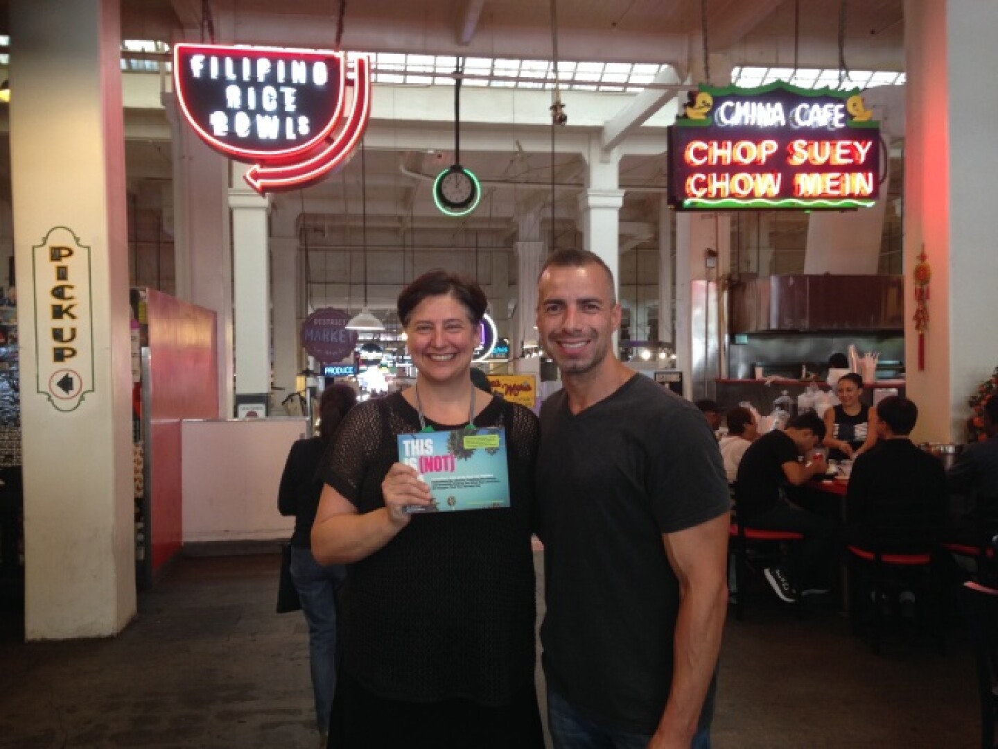 A Martinez stands with author Jen Bilik at Grand Central Market in downtown L.A. with neon restaurant signs behind them.