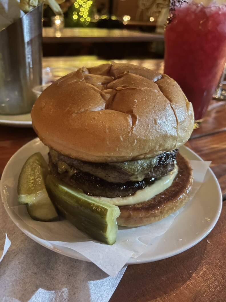 A small plate with a burger and pickles on the side.