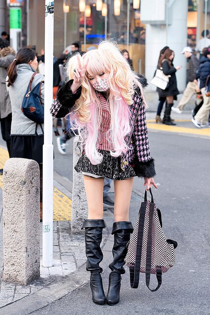 A young girl in Shibuya, Tokyo, poses for a photographer wearing a decorated surgical mask. In Japan, wearing a mask after being sick is considered common practice out of courtesy for others.