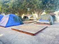 A plywood platform on the dirt ground, surrounded by canvas tents
