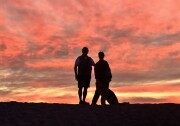 A man and woman backlit against a brilliant sunset at the ocean.