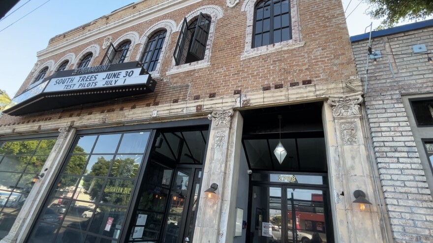 An image of the outside of an old brick two-story building with large glass windows on the first floor.