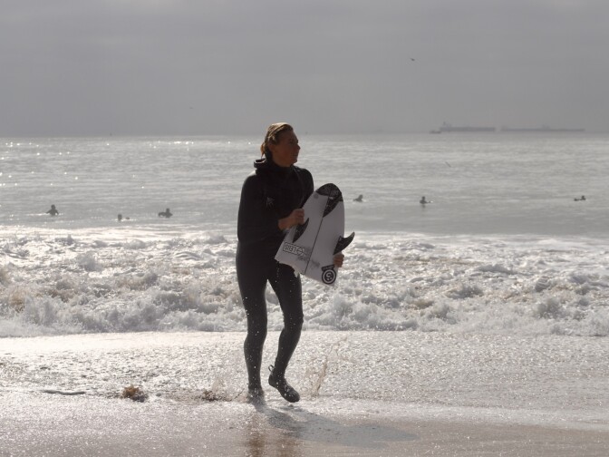 A surfer holds the back half of a broken board on shore
