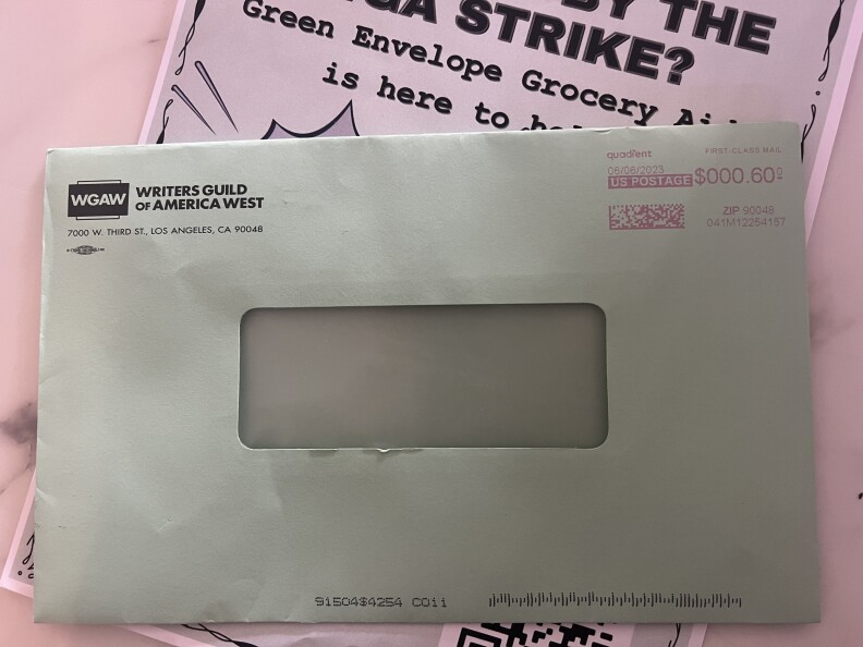 A green colored envelope with an empty window lies on a pink strike flyer. On the envelope it says Writers Guild of America West in black