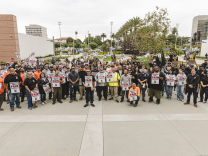 A group of people holding union signs and flags stands in front of a government building. 