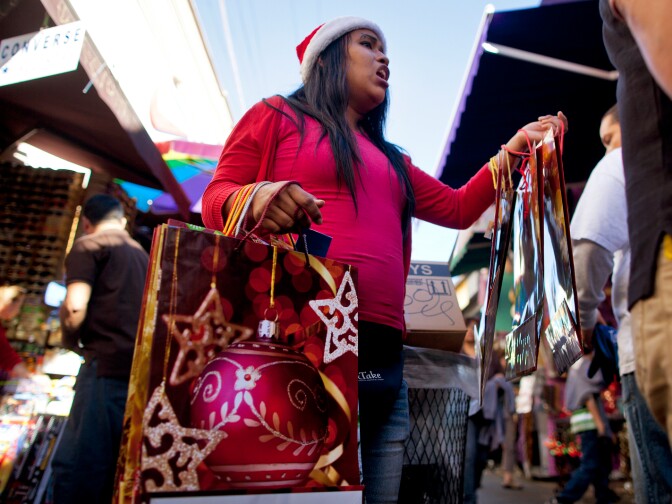 Daisy Benitez sells holiday-themed gift bags in Santee Alley as shoppers buy last-minute gifts on Christmas Eve.